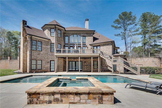 rear view of property with a balcony, a swimming pool with hot tub, and a patio area