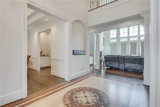 foyer entrance featuring ornamental molding, decorative columns, wood-type flooring, and a high ceiling