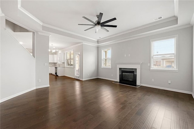 unfurnished living room featuring dark hardwood / wood-style flooring, a raised ceiling, ceiling fan with notable chandelier, and crown molding