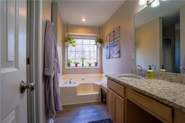 full bath featuring a textured ceiling, vanity, a garden tub, and wood finished floors