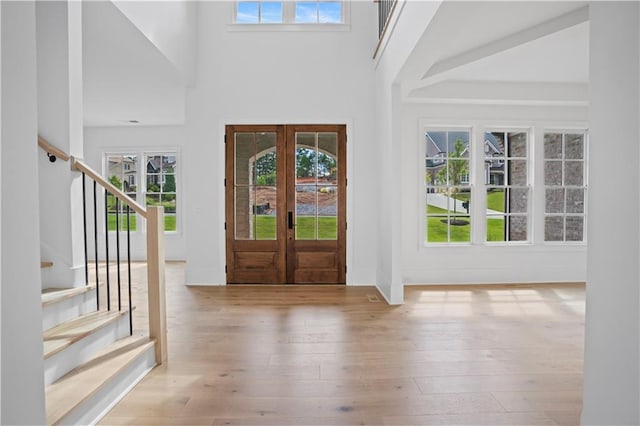 foyer entrance with french doors, light hardwood / wood-style floors, and a high ceiling