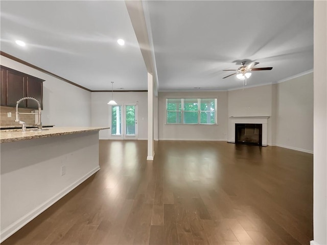unfurnished living room with a ceiling fan, dark wood-style flooring, ornamental molding, a fireplace, and a sink