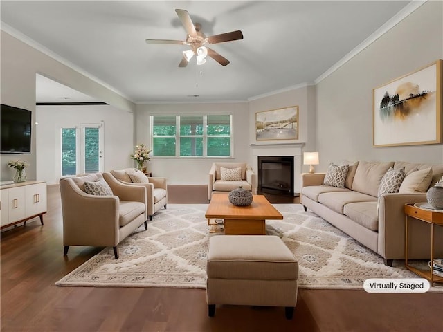 living area with crown molding, a ceiling fan, a glass covered fireplace, and wood finished floors