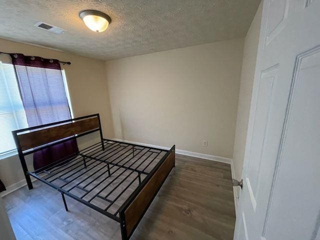bedroom featuring a textured ceiling, wood finished floors, visible vents, and baseboards