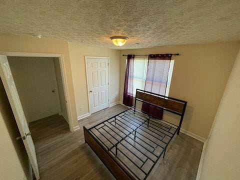 unfurnished bedroom with a textured ceiling, wood finished floors, and baseboards