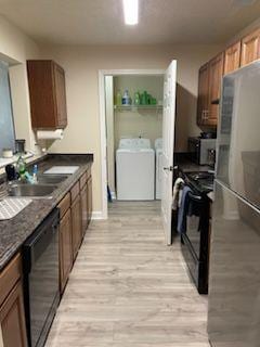 kitchen featuring dark countertops, light wood-style flooring, a sink, independent washer and dryer, and black appliances