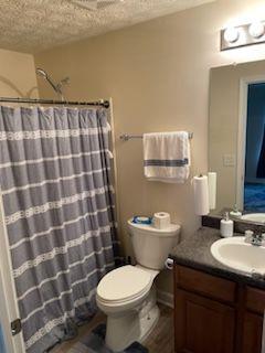 full bath with a shower with curtain, vanity, toilet, and a textured ceiling