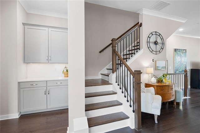 stairs with baseboards, wood finished floors, visible vents, and ornamental molding