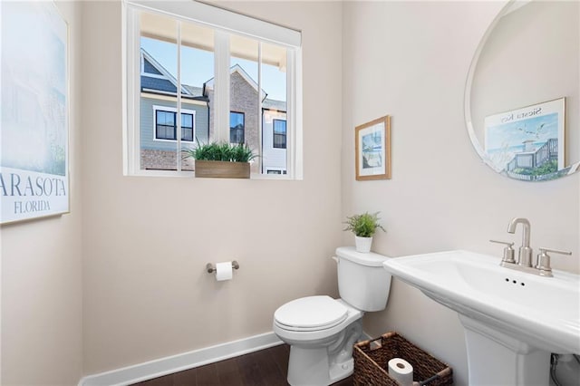 half bathroom featuring wood finished floors, toilet, baseboards, and a sink