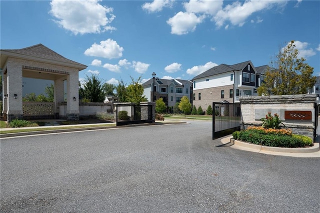 view of road featuring a gate, curbs, a residential view, and a gated entry