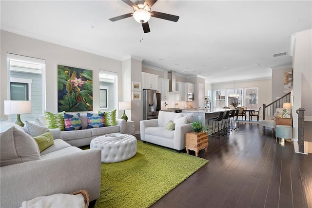 living area featuring visible vents, dark wood-type flooring, stairs, ornamental molding, and ceiling fan with notable chandelier