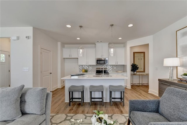 kitchen featuring decorative light fixtures, stainless steel appliances, a kitchen bar, a kitchen island with sink, and white cabinetry