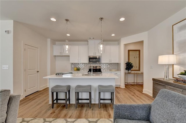 kitchen featuring a kitchen island with sink, appliances with stainless steel finishes, a breakfast bar, white cabinetry, and decorative light fixtures