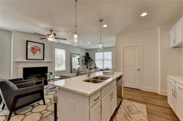 kitchen featuring dishwasher, a kitchen island with sink, sink, white cabinetry, and decorative light fixtures