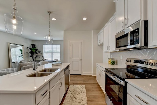 kitchen featuring stainless steel appliances, an island with sink, hanging light fixtures, sink, and white cabinetry