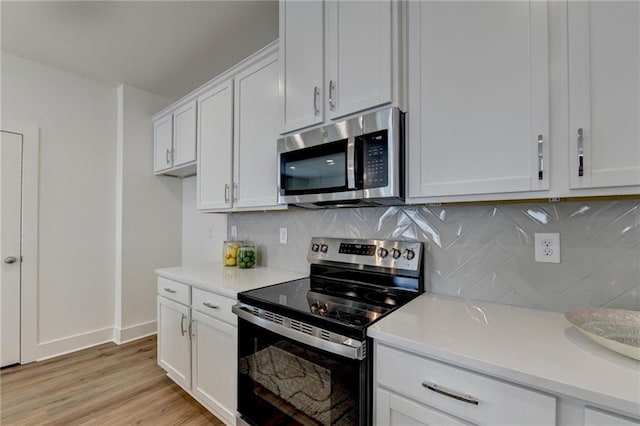 kitchen with white cabinets, appliances with stainless steel finishes, backsplash, and light hardwood / wood-style flooring