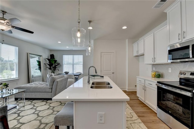 kitchen with pendant lighting, stainless steel appliances, a center island with sink, white cabinets, and sink