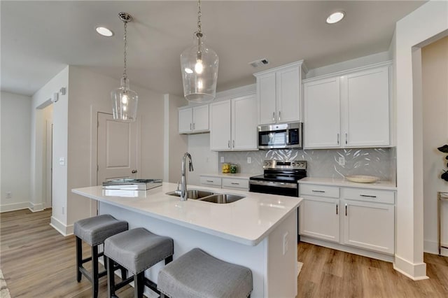 kitchen featuring stainless steel appliances, sink, white cabinetry, backsplash, and a kitchen island with sink