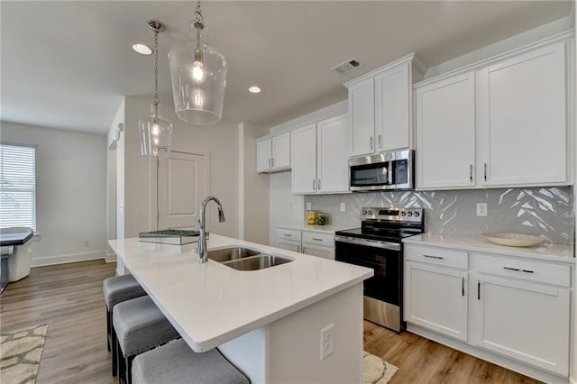 kitchen featuring a center island with sink, appliances with stainless steel finishes, hanging light fixtures, white cabinets, and sink