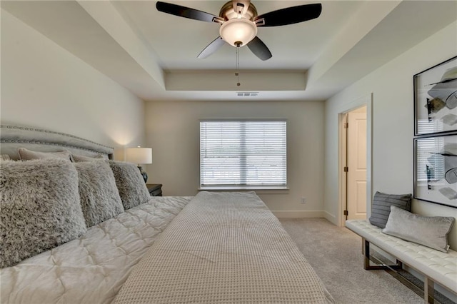 bedroom with ceiling fan, a tray ceiling, and light carpet