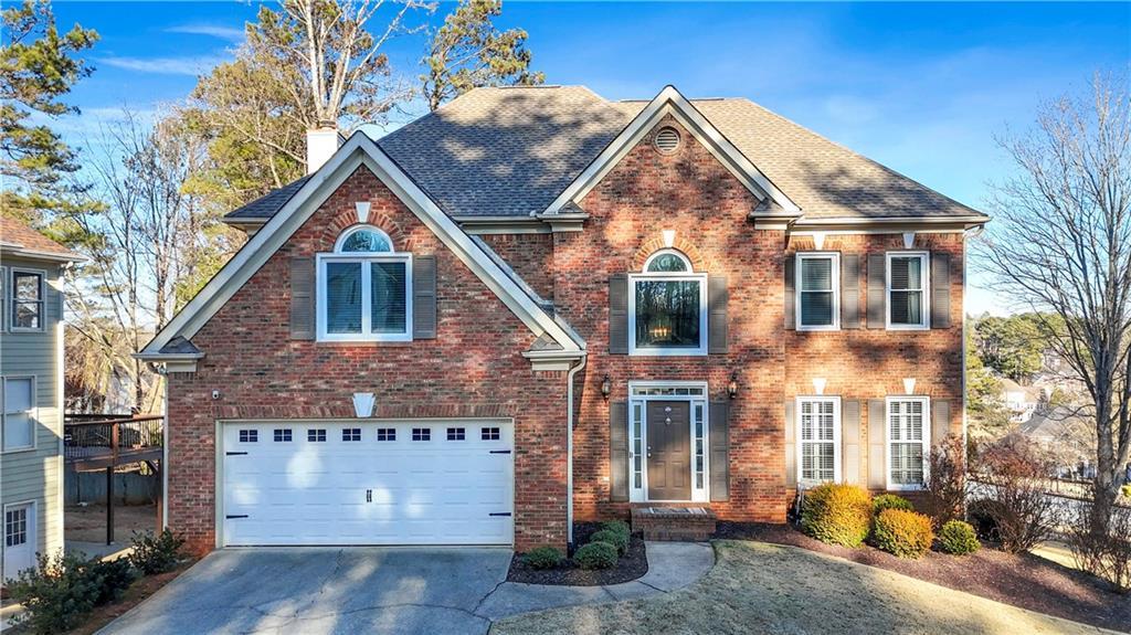 view of front of house with driveway, a chimney, roof with shingles, an attached garage, and brick siding