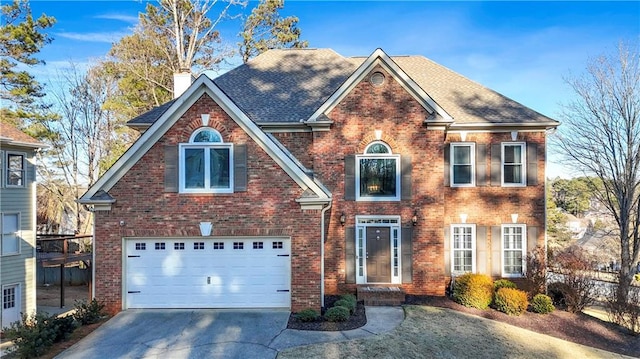 view of front of house with driveway, a chimney, roof with shingles, an attached garage, and brick siding