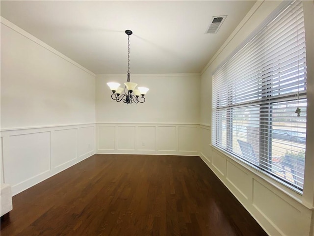 unfurnished dining area featuring dark wood-style flooring, a wainscoted wall, visible vents, an inviting chandelier, and ornamental molding