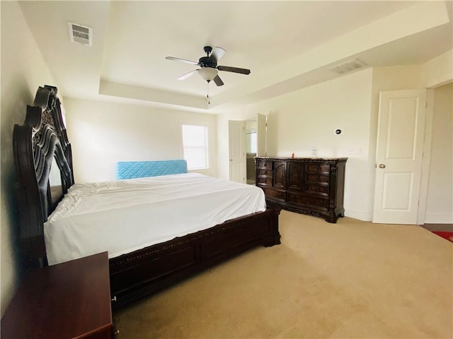 bedroom featuring light colored carpet, a tray ceiling, visible vents, and a ceiling fan