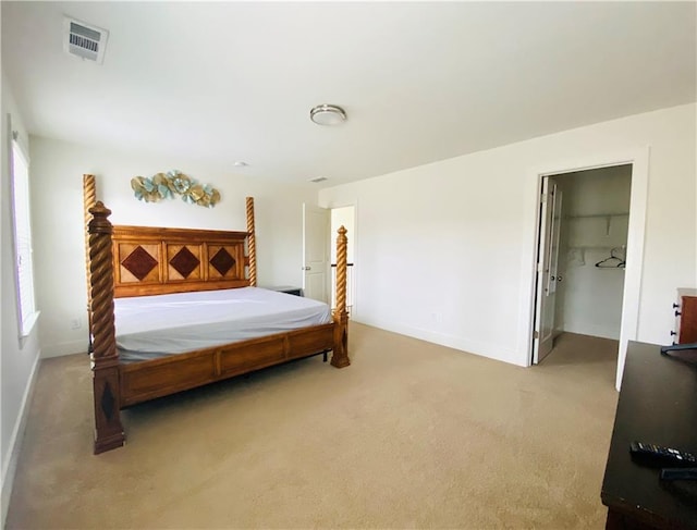 bedroom featuring baseboards, a walk in closet, visible vents, and light colored carpet