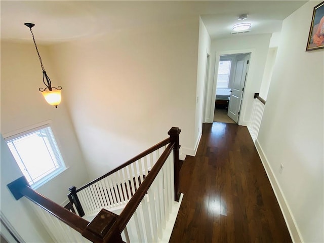 hall featuring dark wood-style floors, baseboards, a wealth of natural light, and an upstairs landing