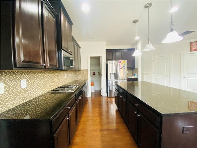 kitchen featuring stainless steel appliances, wood finished floors, a kitchen island, decorative backsplash, and dark stone countertops