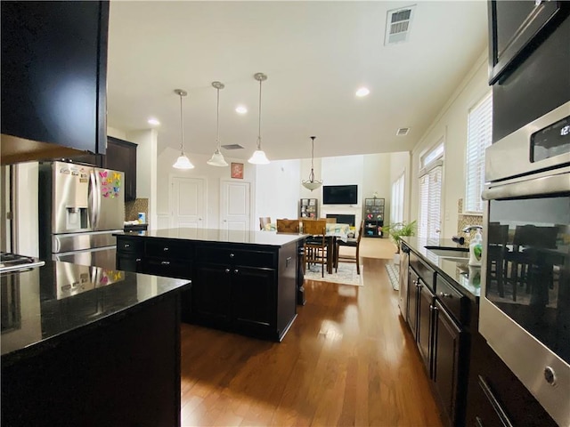 kitchen featuring a center island, dark wood finished floors, stainless steel appliances, visible vents, and dark cabinetry