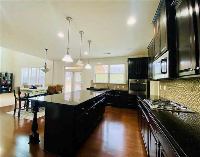 kitchen with decorative backsplash, appliances with stainless steel finishes, dark wood-style flooring, dark cabinetry, and a kitchen bar