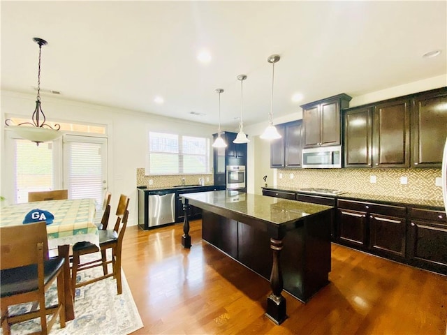 kitchen with stainless steel appliances, a sink, a kitchen island, dark wood-style floors, and tasteful backsplash