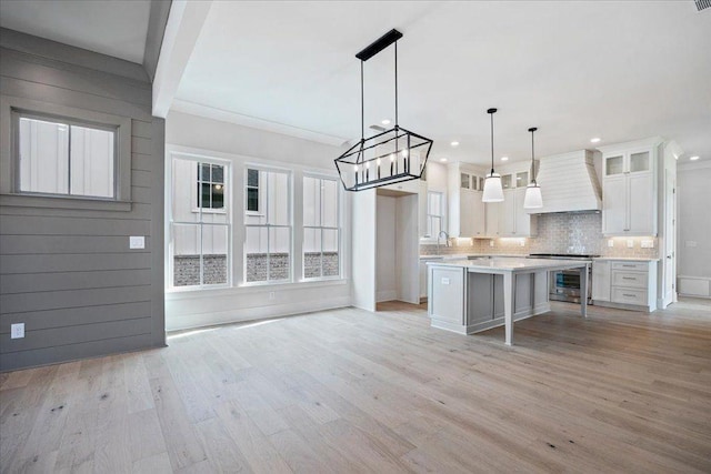 kitchen featuring light countertops, custom range hood, backsplash, light wood-style floors, and white cabinetry