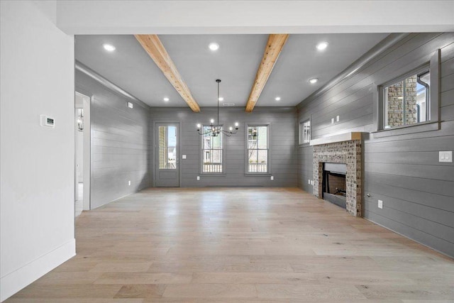 unfurnished living room with beamed ceiling, an inviting chandelier, light wood-style floors, a fireplace, and recessed lighting