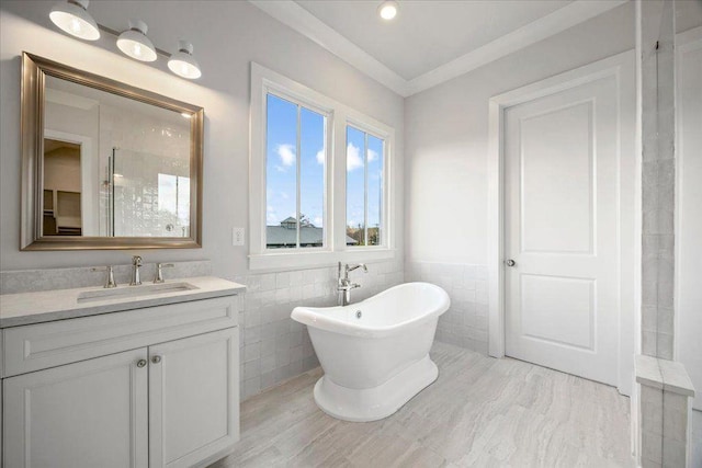 bathroom with a wainscoted wall, crown molding, tile walls, a freestanding bath, and vanity