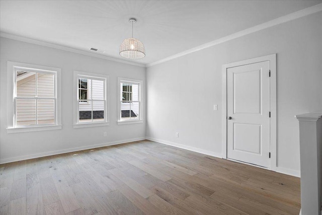 spare room featuring baseboards, visible vents, wood finished floors, and ornamental molding