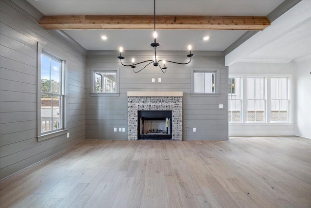 unfurnished living room featuring beamed ceiling, a tiled fireplace, wood finished floors, and an inviting chandelier