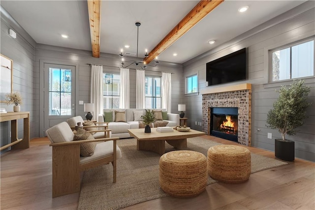 living area featuring beam ceiling, a brick fireplace, wood finished floors, and an inviting chandelier