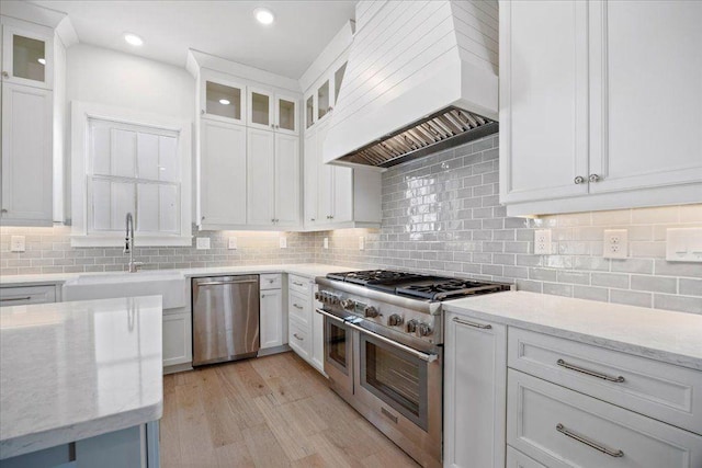 kitchen with appliances with stainless steel finishes, a sink, custom exhaust hood, and light stone countertops