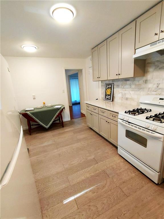 2225 Harold Ln SE, Smyrna, GA 30080 - kitchen featuring white range with gas cooktop, under cabinet range hood, backsplash, light countertops, and light wood-style flooring