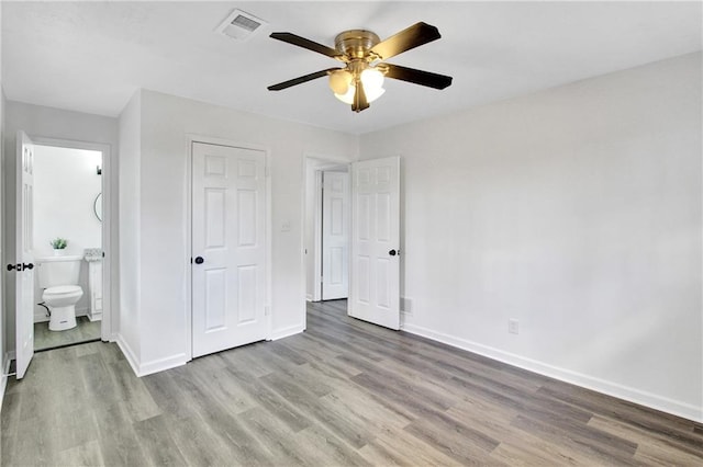 unfurnished bedroom featuring visible vents, wood finished floors, connected bathroom, baseboards, and ceiling fan