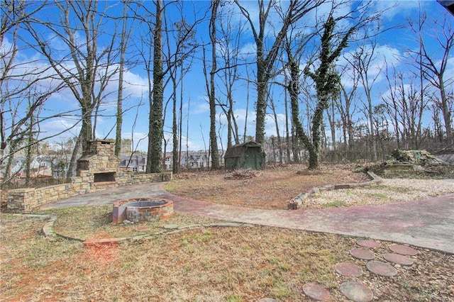 view of yard featuring an outbuilding, an outdoor stone fireplace, a storage shed, and a patio area