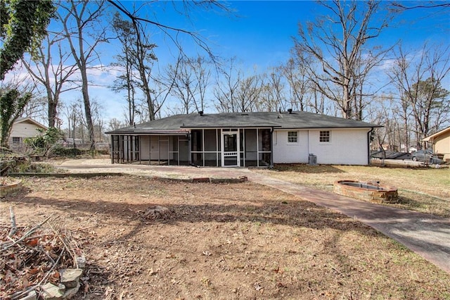 back of property with a sunroom, a yard, and a fire pit