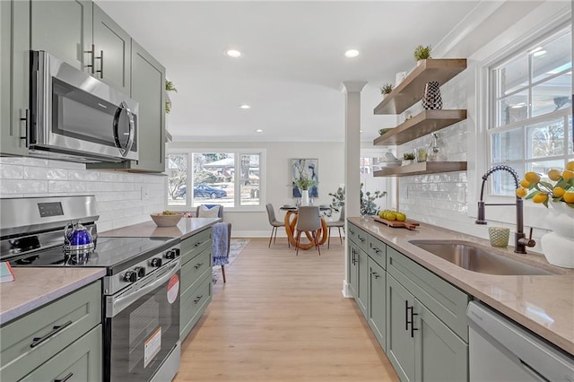 kitchen with appliances with stainless steel finishes, tasteful backsplash, light wood-type flooring, ornamental molding, and sink