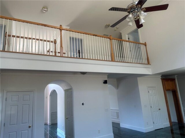 interior space with crown molding, a towering ceiling, baseboards, ceiling fan, and arched walkways