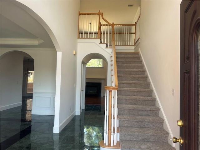 entrance foyer featuring crown molding, a fireplace, baseboards, visible vents, and stairway