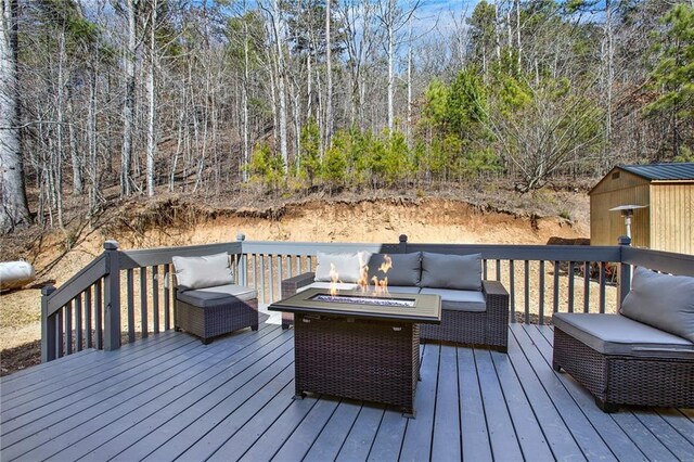 deck with an outdoor living space with a fire pit, an outbuilding, a wooded view, and a storage shed