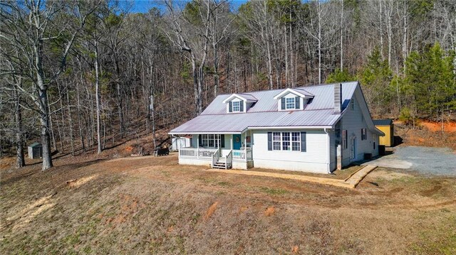 view of front of property featuring a front yard, an outbuilding, a forest view, covered porch, and metal roof